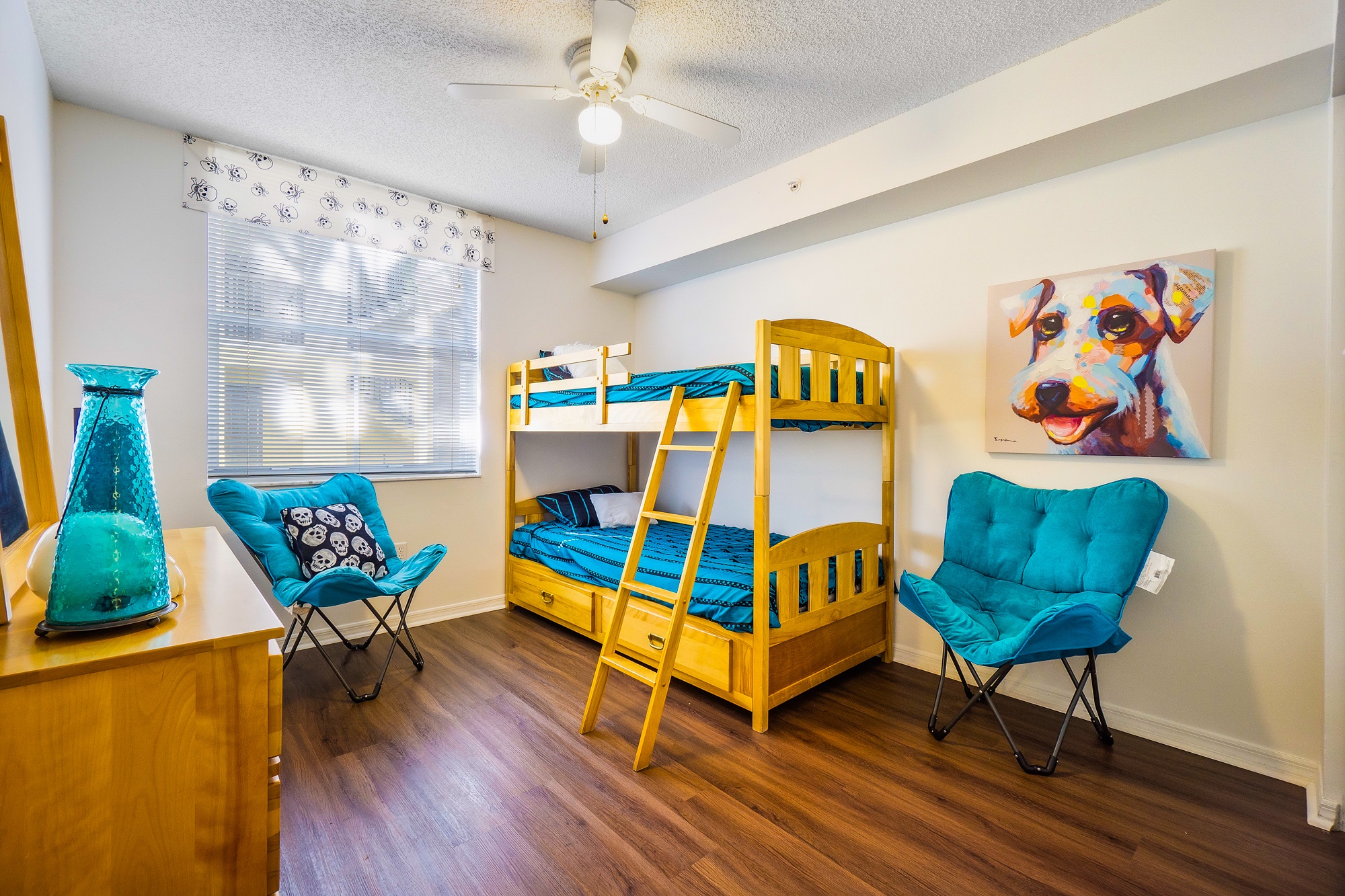 A room with a bunk bed, a chair, and a painting of a dog.
